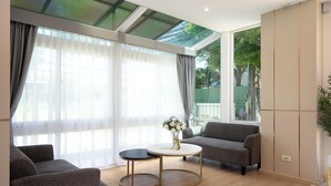 A modern living room with a sofa, a round coffee table, and a large window with sheer curtains. - Riski Residence (Nonthaburi)