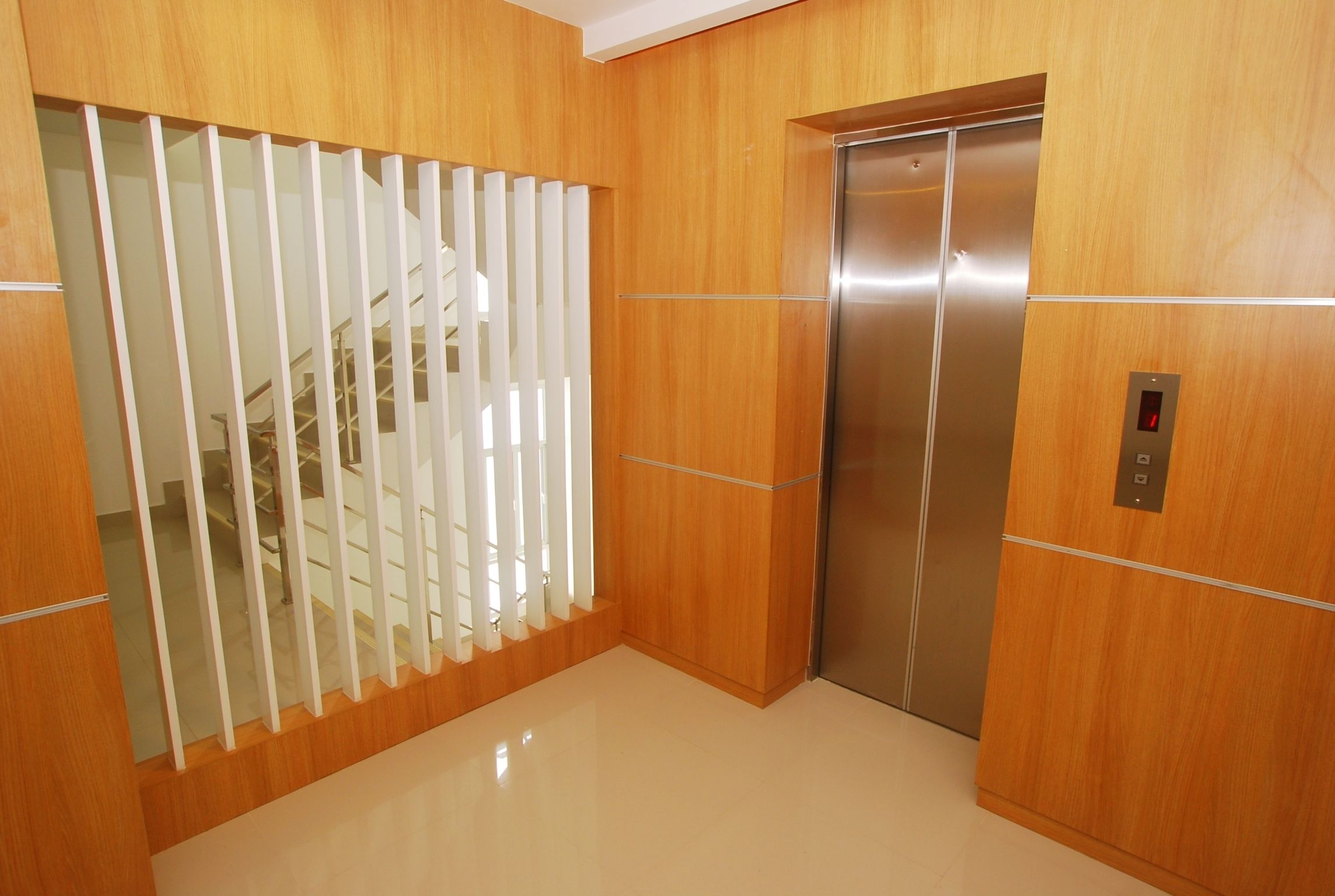 Een moderne lift met een metalen afwerking, naast een houten wand en een wit scheidingswand met verticale latten.