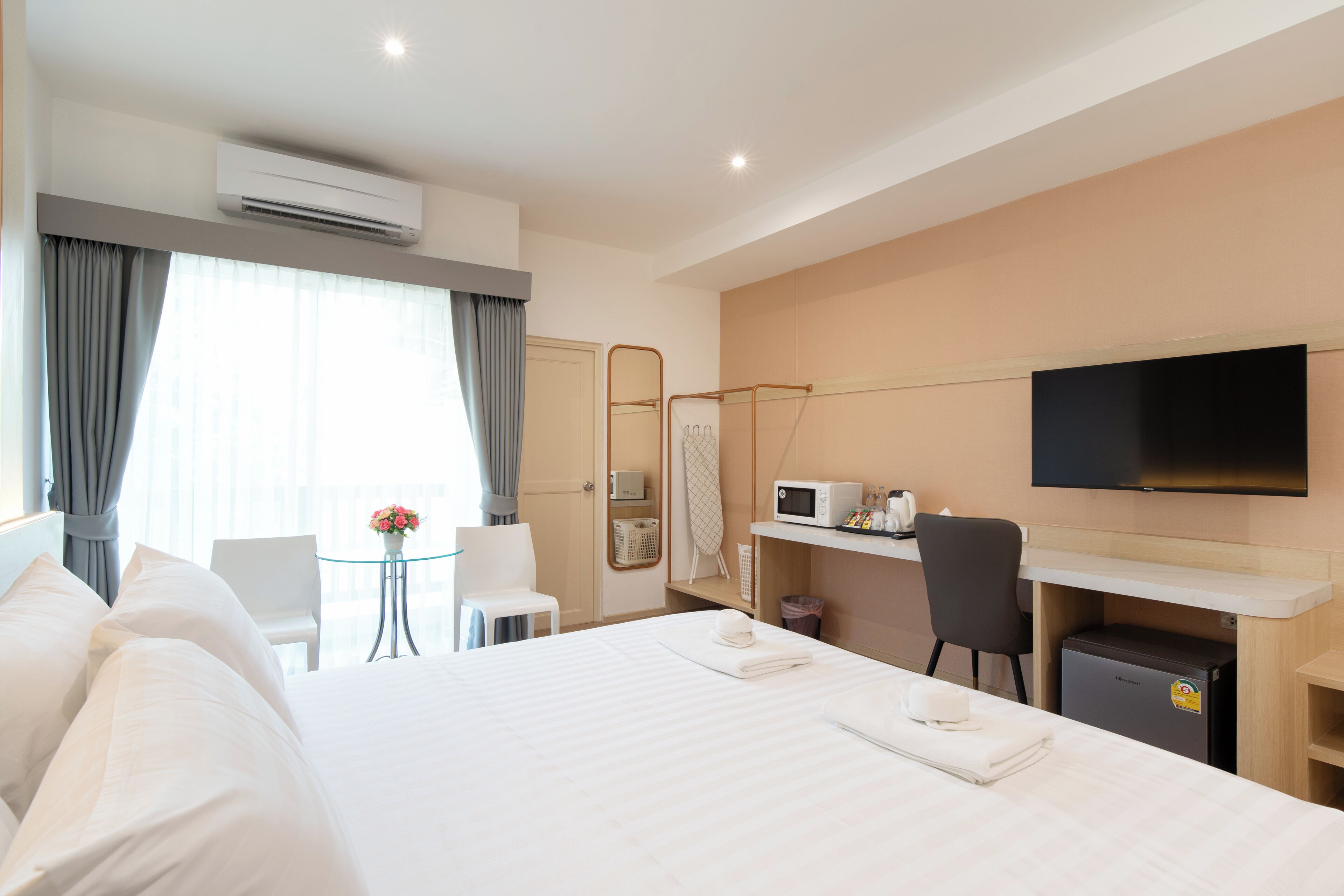A hotel room with a bed, a desk, a chair, a TV, and an air conditioning unit.