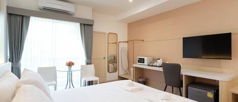 A hotel room with a bed, a desk, a chair, a TV, and an air conditioning unit.