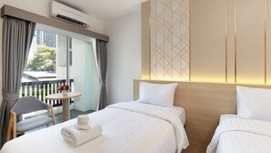 A hotel room with two beds, a small table, a chair, and a view of the outdoors. - Riski Residence (Nonthaburi)