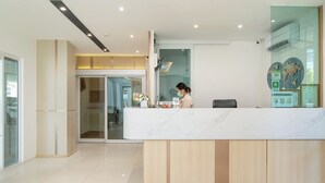 A modern reception area with a marble counter, wooden paneling, and a glass door leading to a waiting area. - Riski Residence (Nonthaburi)