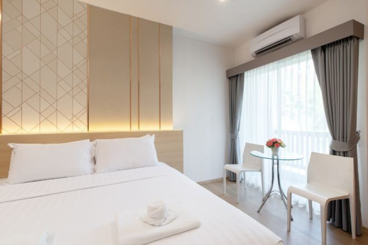 A hotel room with a large bed, a small table with chairs, and a balcony with curtains.