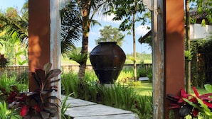 A wooden pathway leading to a decorative archway with intricate carvings, surrounded by lush tropical plants and a large decorative pot. - MATHIS Retreat Ubud (Ubud)