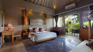 A spacious bedroom with a large bed, a wooden nightstand, a desk, and a chair. There is a view of the outdoors through a large window. - MATHIS Retreat Ubud (Ubud)