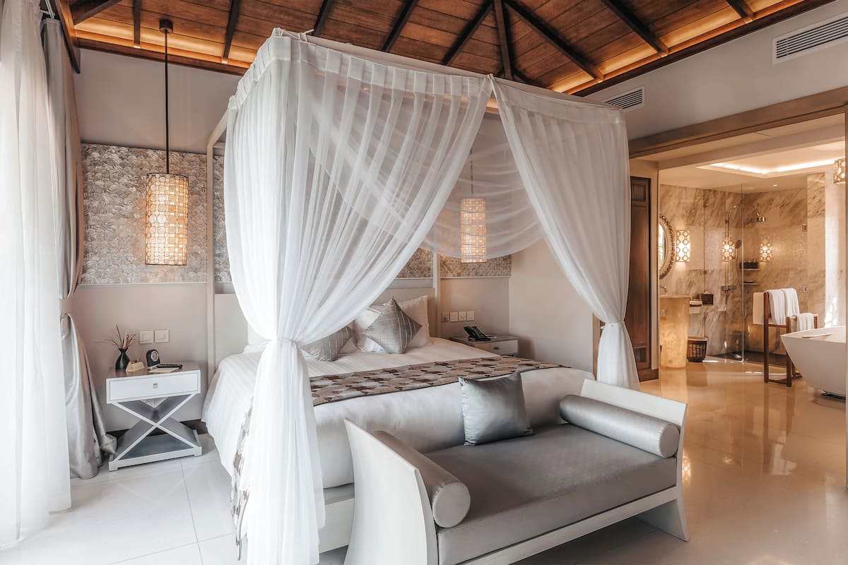 Ein Schlafzimmer mit Baldachinbett, Nachttisch, Sofa und einem Badezimmer mit Badewanne und Dusche.