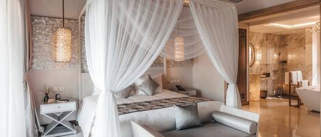 Une chambre à coucher avec un lit à baldaquin, une table de chevet, une commode, un canapé et une salle de bain dotée d’une baignoire et d’une douche.