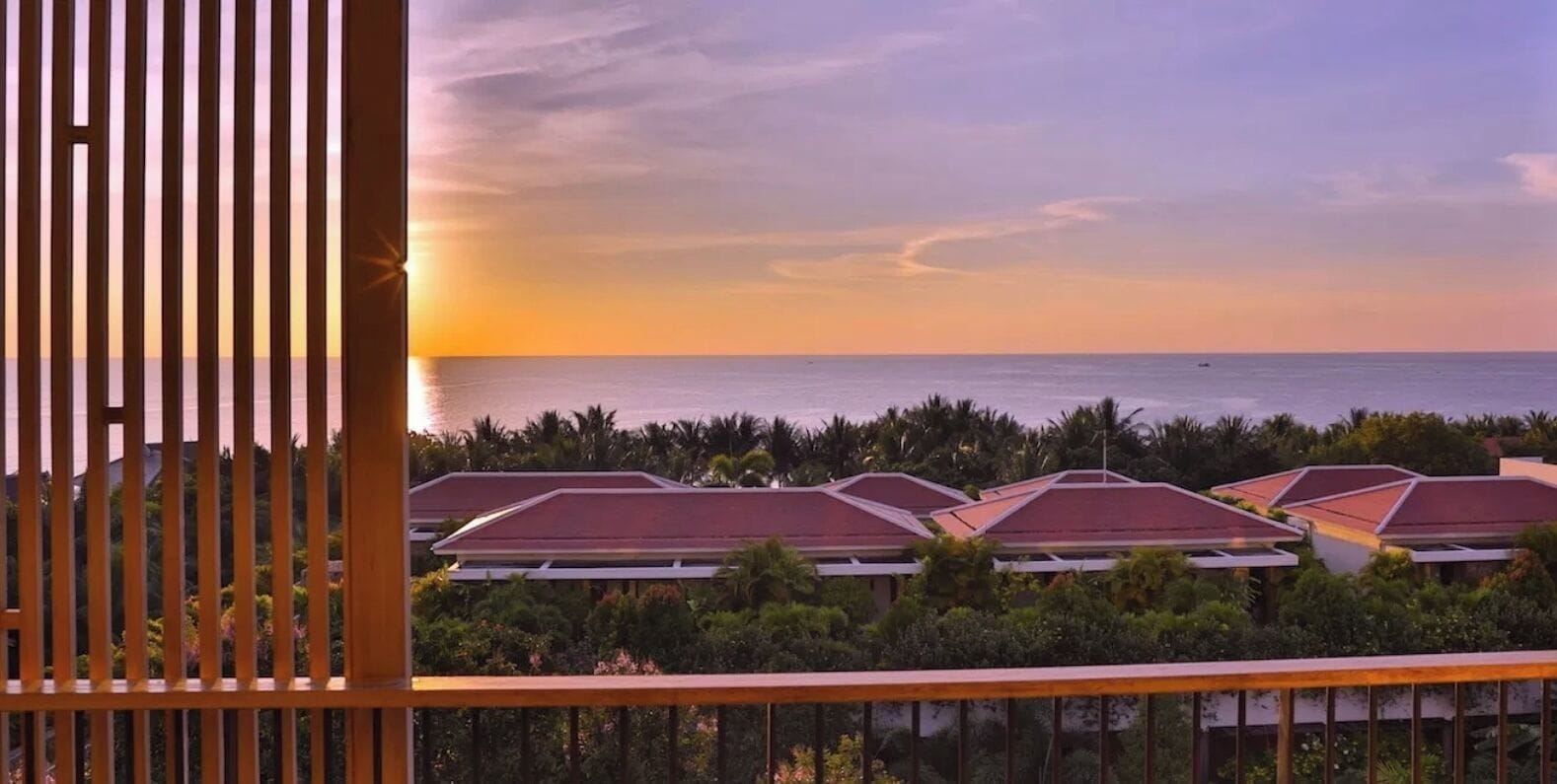 A coastal hotel with multiple buildings, a sunset view, and a balcony with a wooden railing.