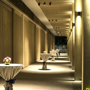 A corridor with evenly spaced tables, each with a white tablecloth and a vase of flowers.