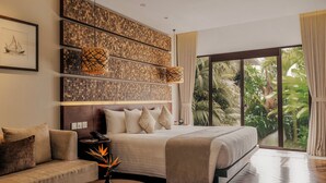 Un dormitorio con cama, sofá, mesa de centro, pared con paneles trenzados y un ventanal con vistas al verdor.