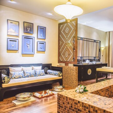 A modern hotel room with a sofa, a small table, a decorative screen, and framed artwork on the wall.