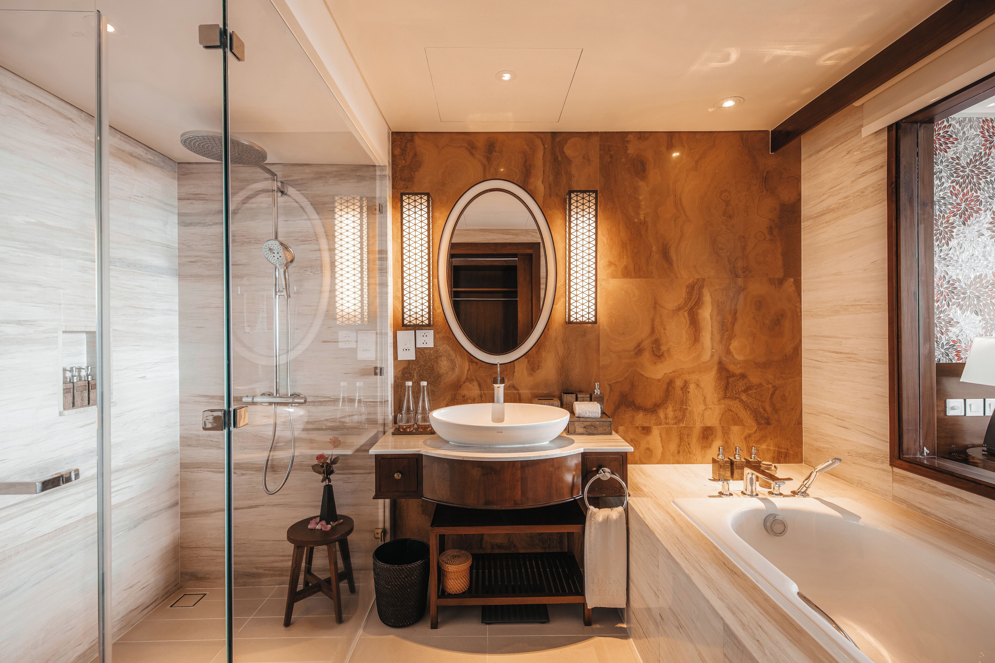 A modern bathroom with a glass-enclosed shower, a large oval mirror, a vessel sink, and a freestanding bathtub.