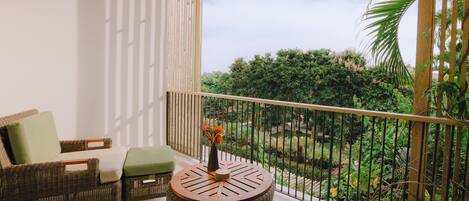 A balcony with wicker furniture, a round table, and a view of greenery.