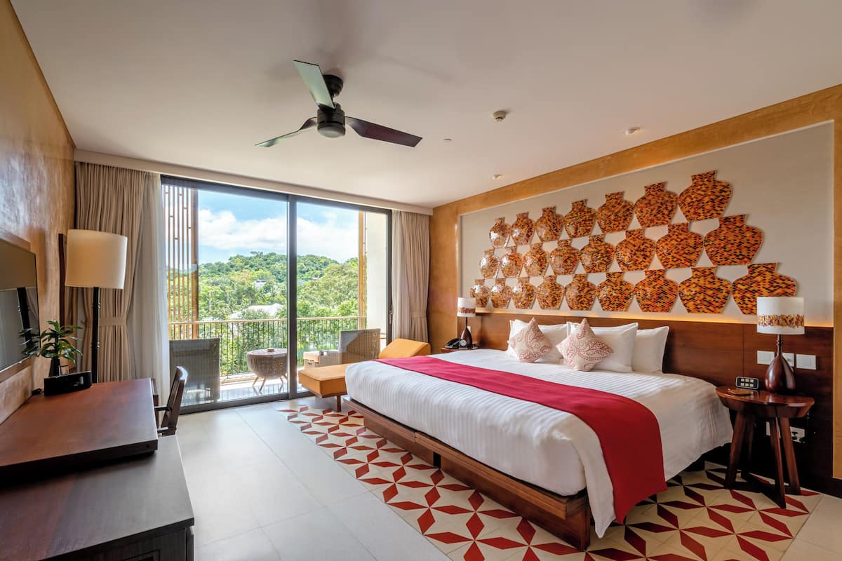 Ein modernes Hotelzimmer mit einem großen Bett, einem Balkon mit Blick, einem Deckenventilator und einer Dekoration an der Wand.