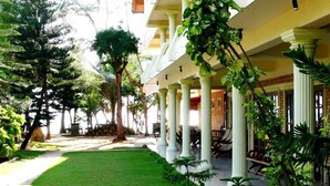 A hotel courtyard with a lawn, potted plants, and a covered seating area with columns. - Time N Tide Beach Resort (Hikkaduwa)
