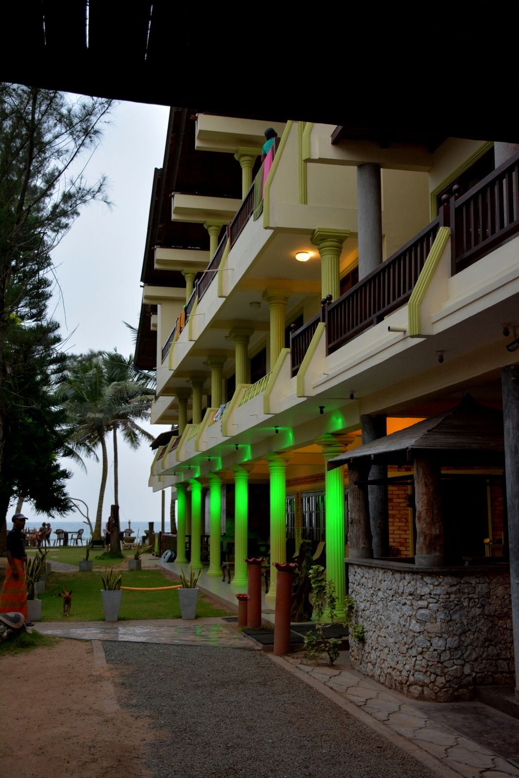 A hotel with multiple balconies, green pillars, and a stone wall.