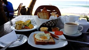 A table with breakfast items including toast, eggs, tomatoes, and a cup of coffee, set against a beach backdrop. - Time N Tide Beach Resort (Hikkaduwa)