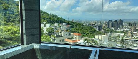 A modern interior with a large window overlooking a cityscape and lush greenery.