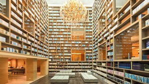 Et rummeligt bibliotek med højt til loftet, en stor lysekrone i midten og reoler med bøger hele vejen rundt.