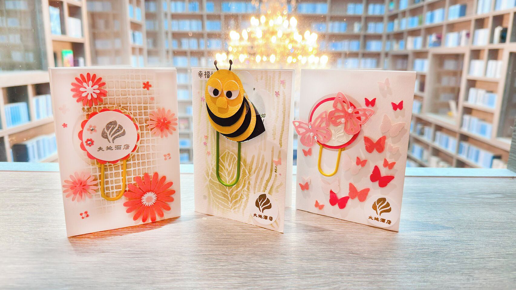 Three greeting cards with floral and bee designs on a wooden surface.