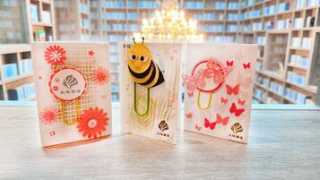 Three greeting cards with floral and bee designs on a wooden surface.