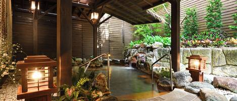A traditional Japanese onsen with a wooden structure, a hot spring, and a rock garden.