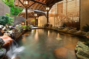Una tranquila fuente interior con un estanque revestido de piedra, vigas de madera y plantas en macetas.