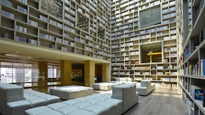 Et rummeligt bibliotek med flere niveauer af bogreoler, behagelige siddeområder og et moderne arkitektonisk design.