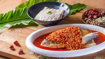Un plato de pescado al vapor con salsa picante, acompañado de un tazón de arroz blanco y un tazón pequeño de salsa de chile.