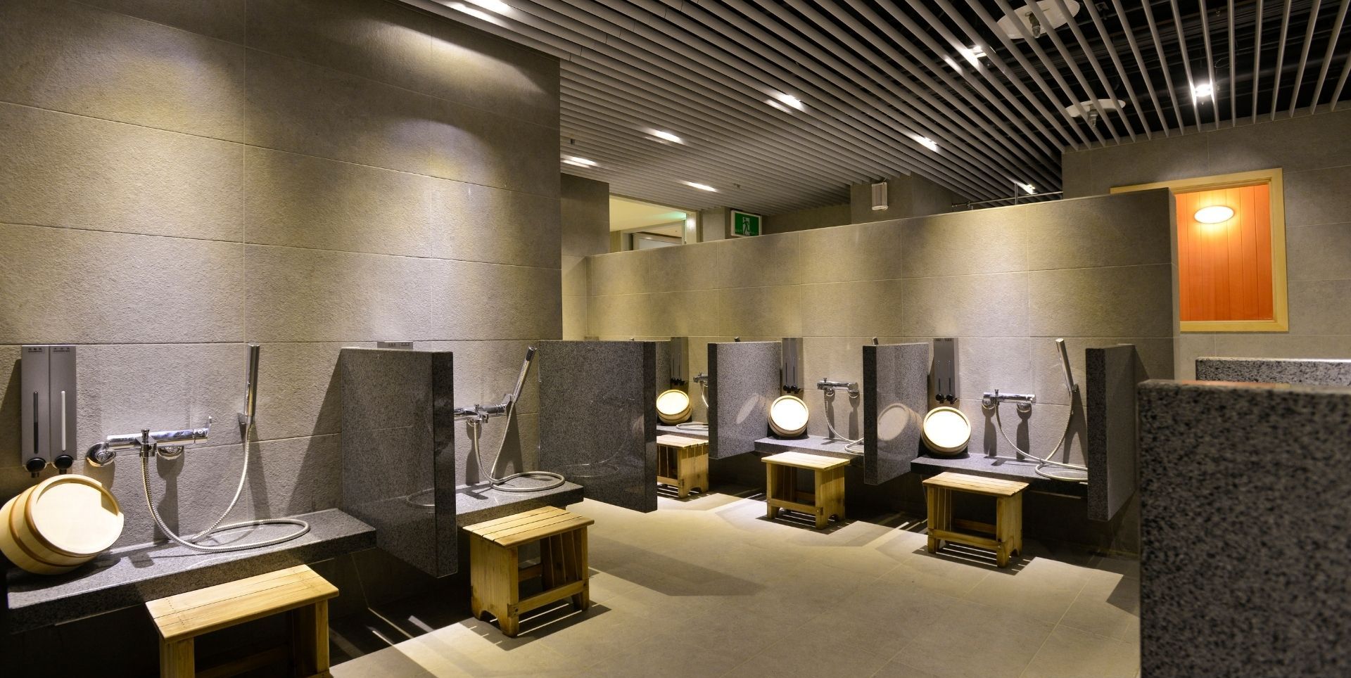 A public hot spring shower area with multiple wooden benches and individual wash stations.