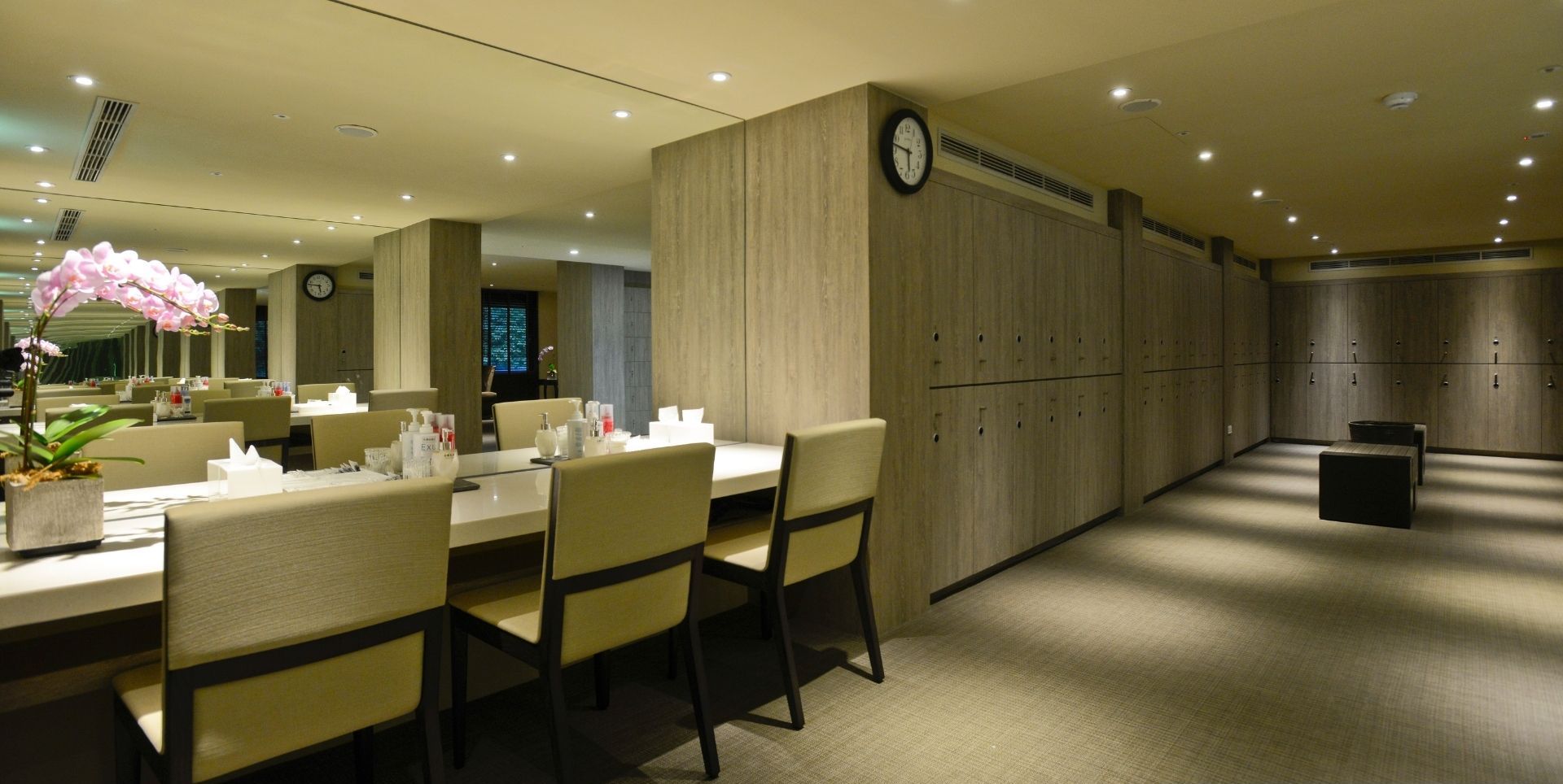 A hotel room with a dining area, a clock on the wall, and a grooming area with lockers.
