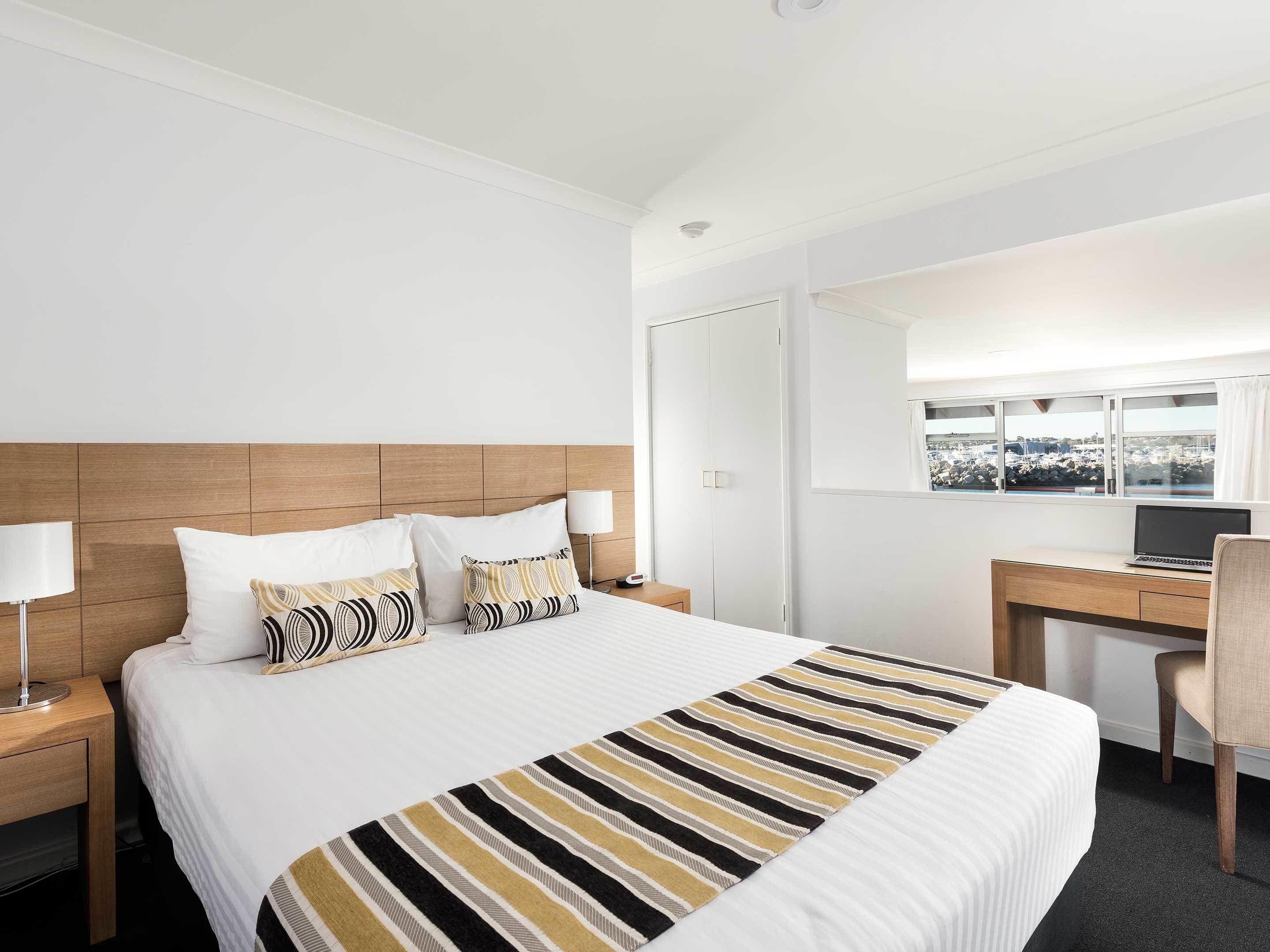A hotel room with a large bed, a desk, a chair, and a window with a city view.