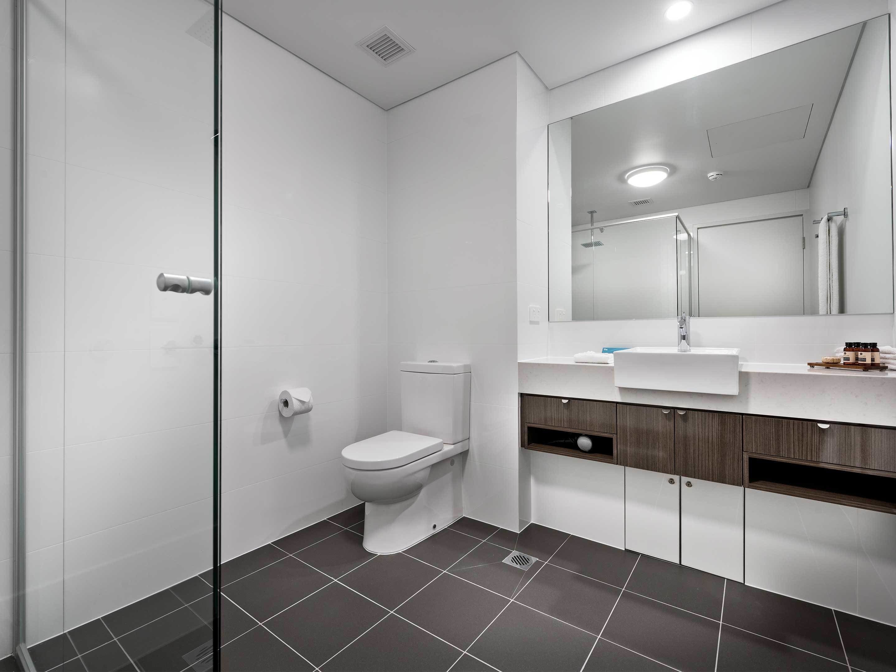 Een moderne badkamer met een douchecabine van glas, toilet, wastafel met spiegel en donkere betegelde vloer.