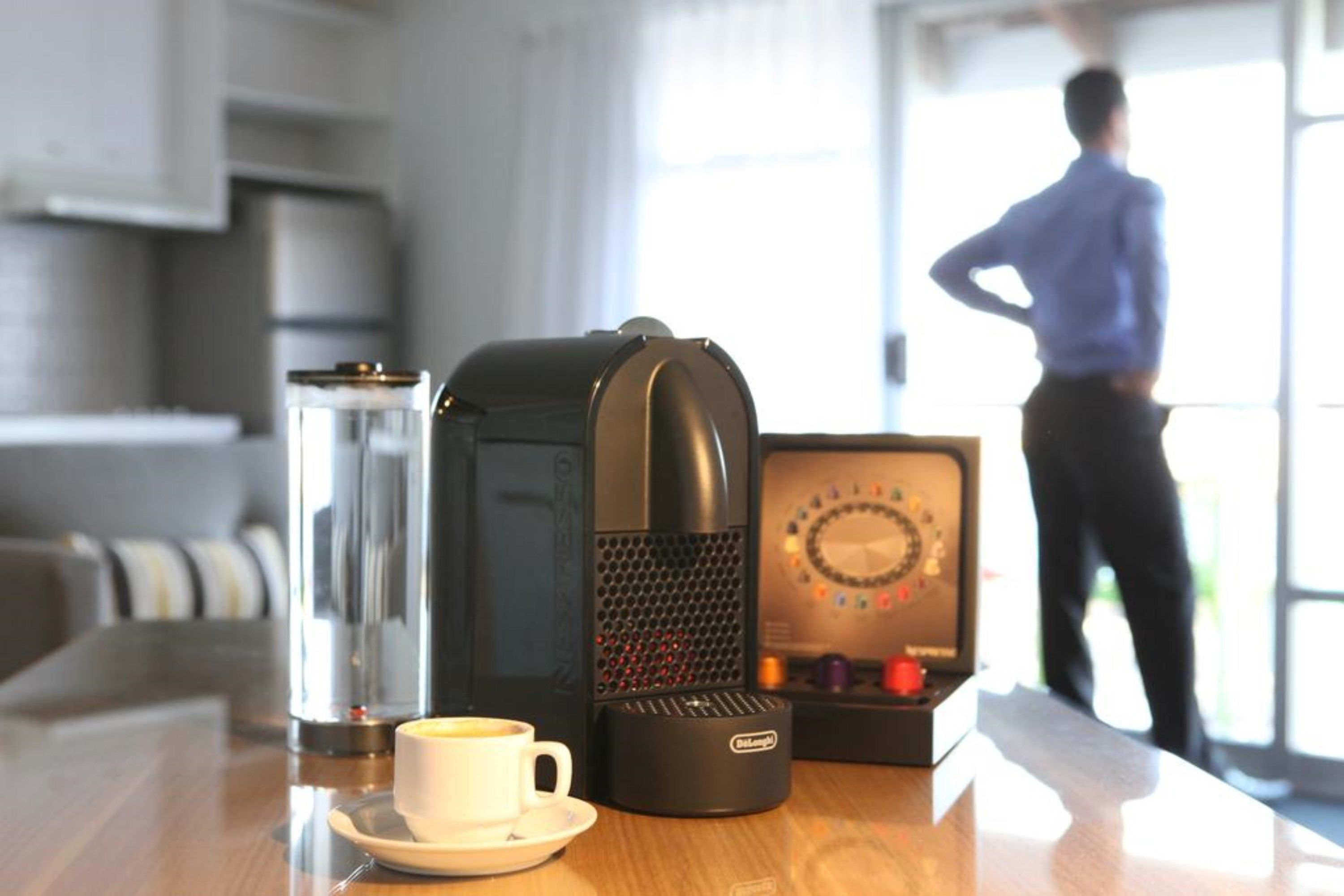 A coffee maker, a cup of coffee, and a box of chocolates on a table.