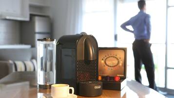 A coffee maker, a cup of coffee, and a box of chocolates on a table.