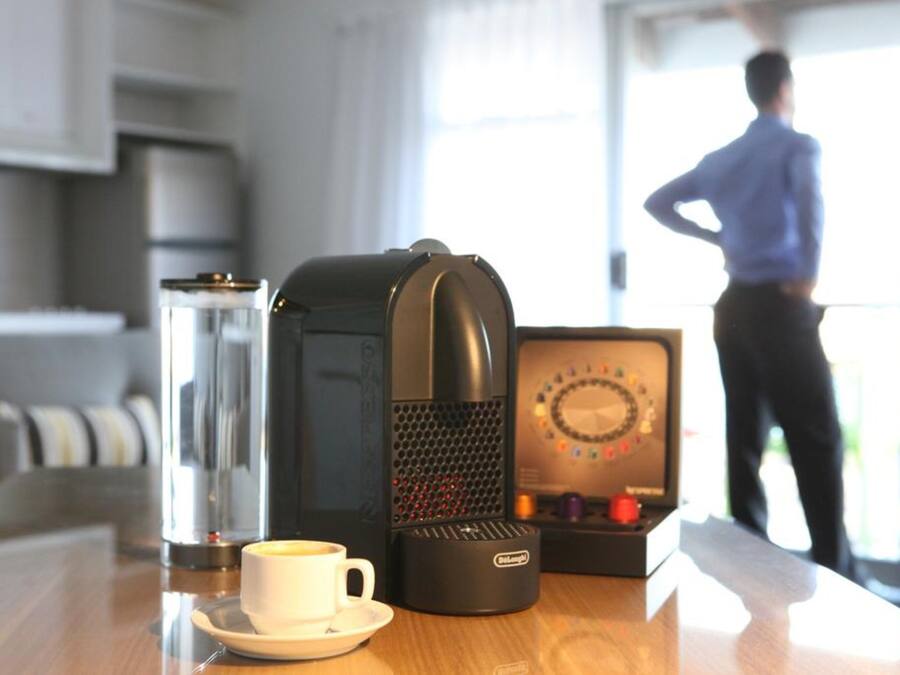 Una cafetera, una taza de café y una caja de bombones sobre una mesa.