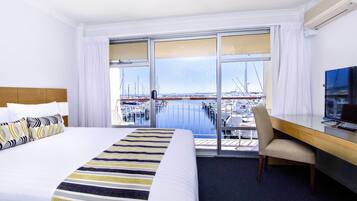 A hotel room with a bed, a desk, a chair, and a TV. The room has a view of a marina with boats.