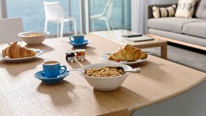 A breakfast table with croissants, coffee, and cereal, overlooking a body of water. - Be. Fremantle (Fremantle)