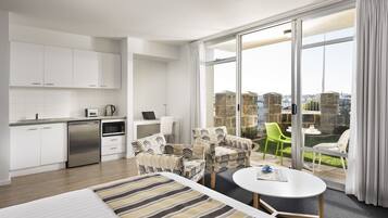 Una habitación de hotel moderna con kitchenette, un comedor con una mesa redonda y un balcón con sillas.