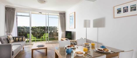 A modern living room with a sofa, a dining table with breakfast, and a TV.