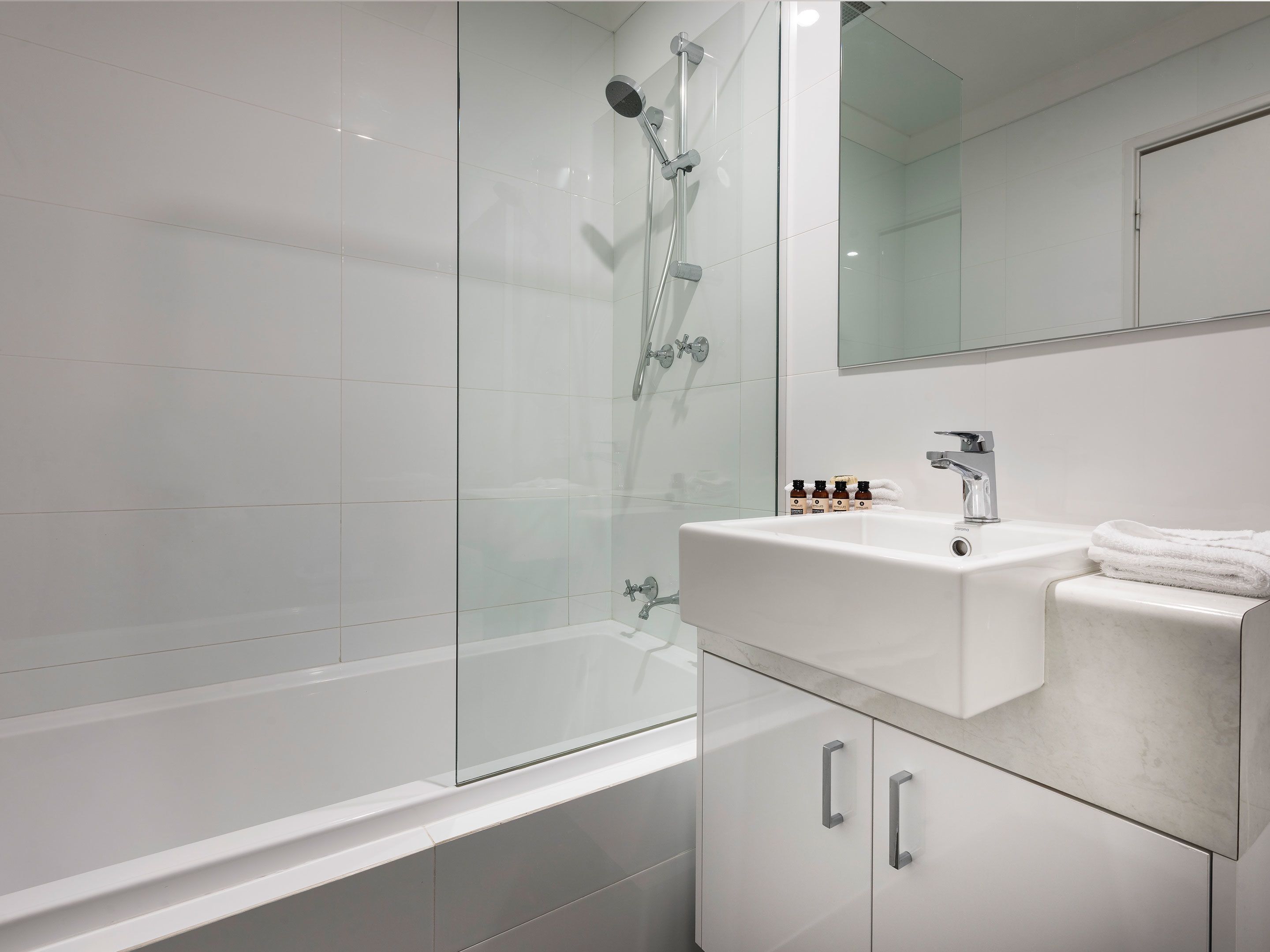 A modern bathroom with a glass-enclosed shower, a white sink with a marble countertop, and a mirror above the sink.