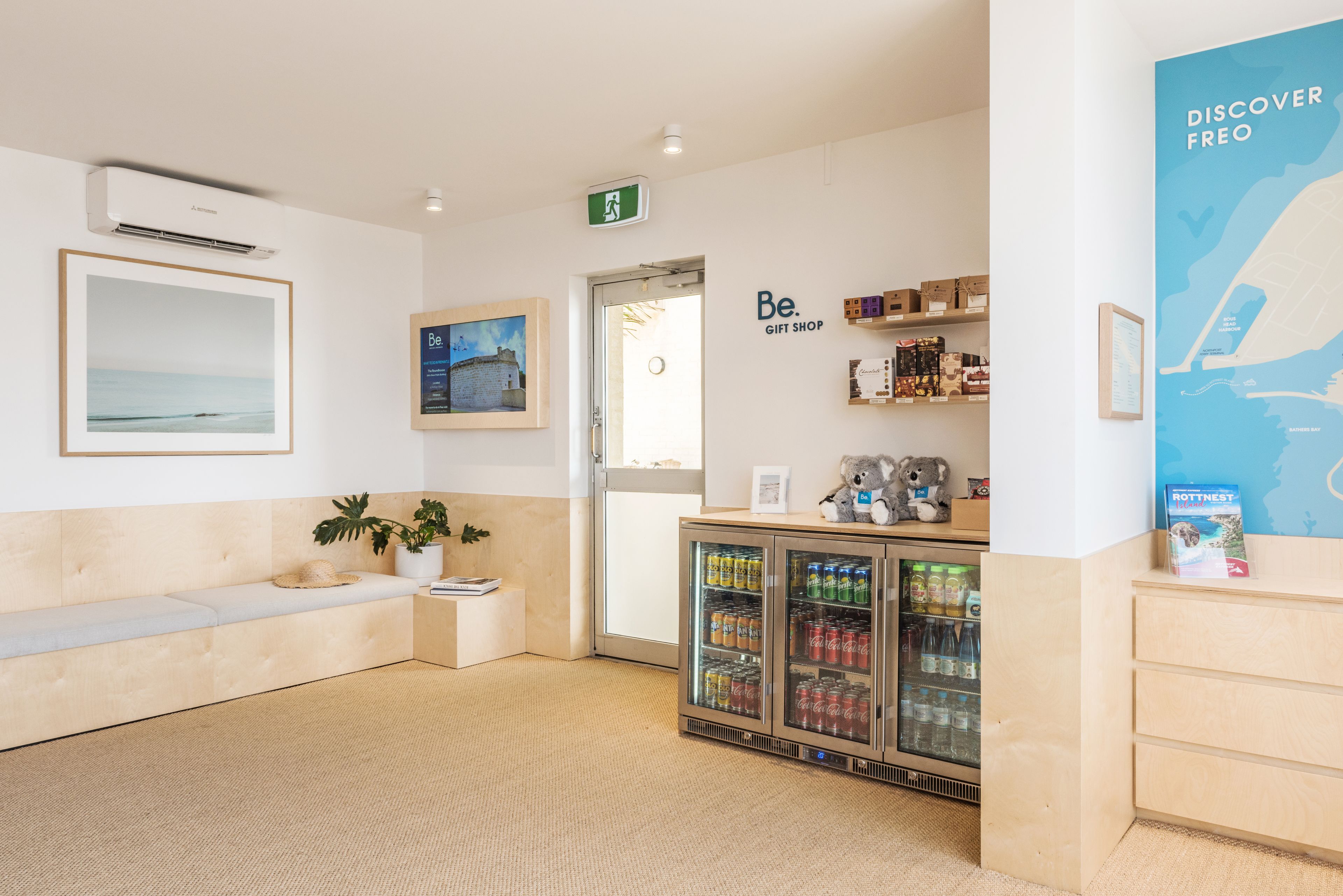 Een modern interieur met een zithoek, een vitrine met drankjes, en een muur met een kaart en tekst.