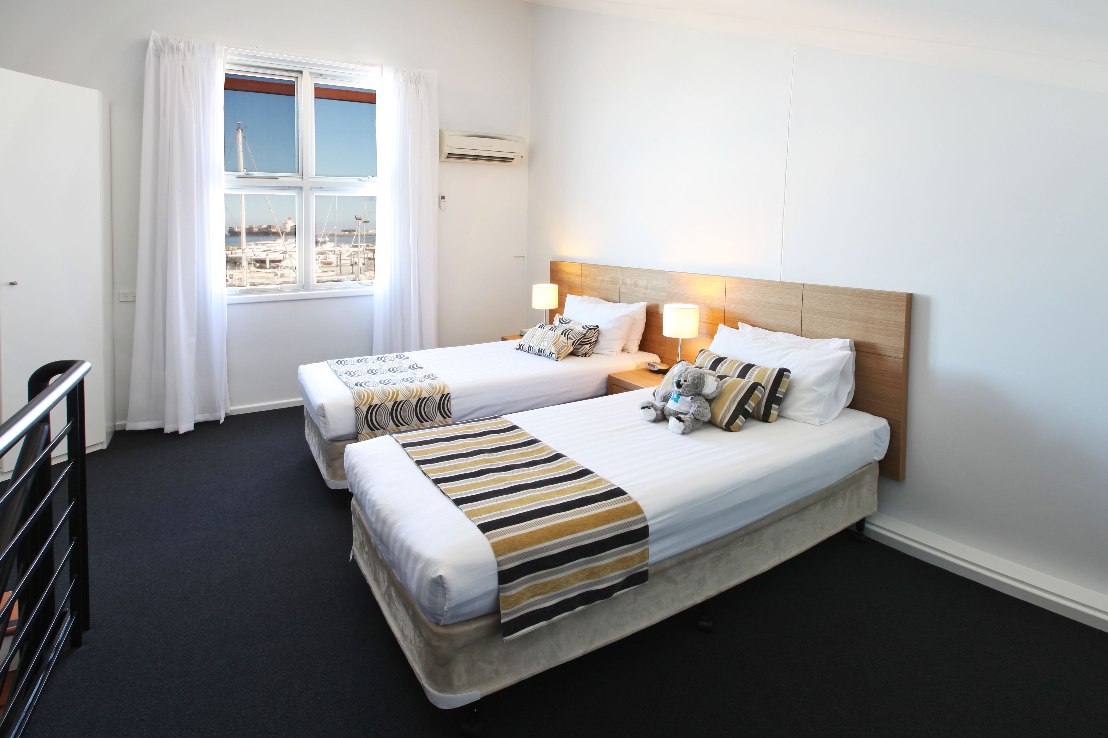 Ein Hotelzimmer mit zwei Betten, einem Fenster mit Blick auf den Yachthafen und einem Holzkopfteil.