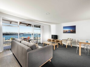 A modern living room with a large window, a sofa, a TV, a small table, and a chair. - Be. Fremantle (Fremantle)