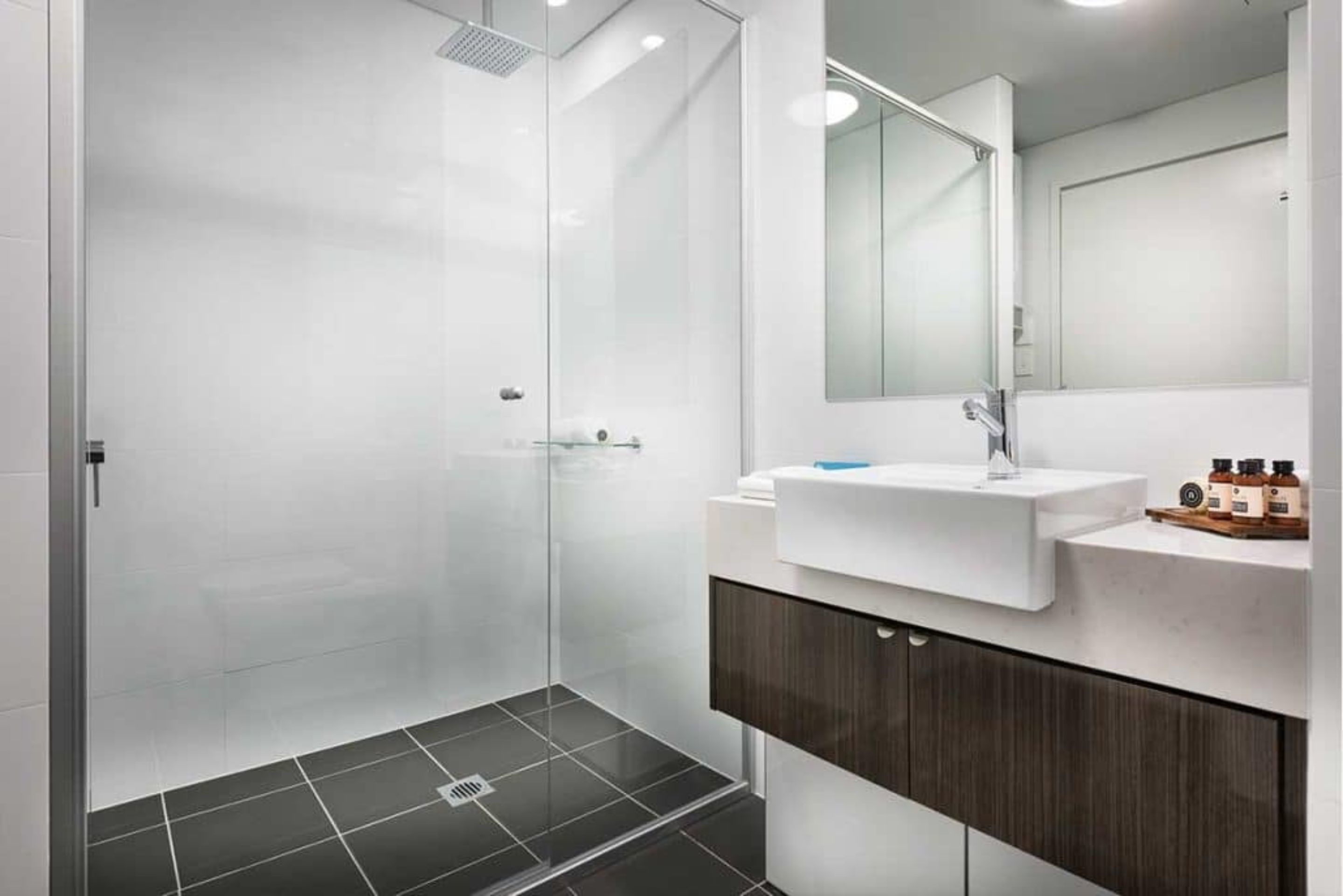 Un baño moderno con cabina de ducha de vidrio, lavamanos blanco y mueble de tocador de madera oscura.