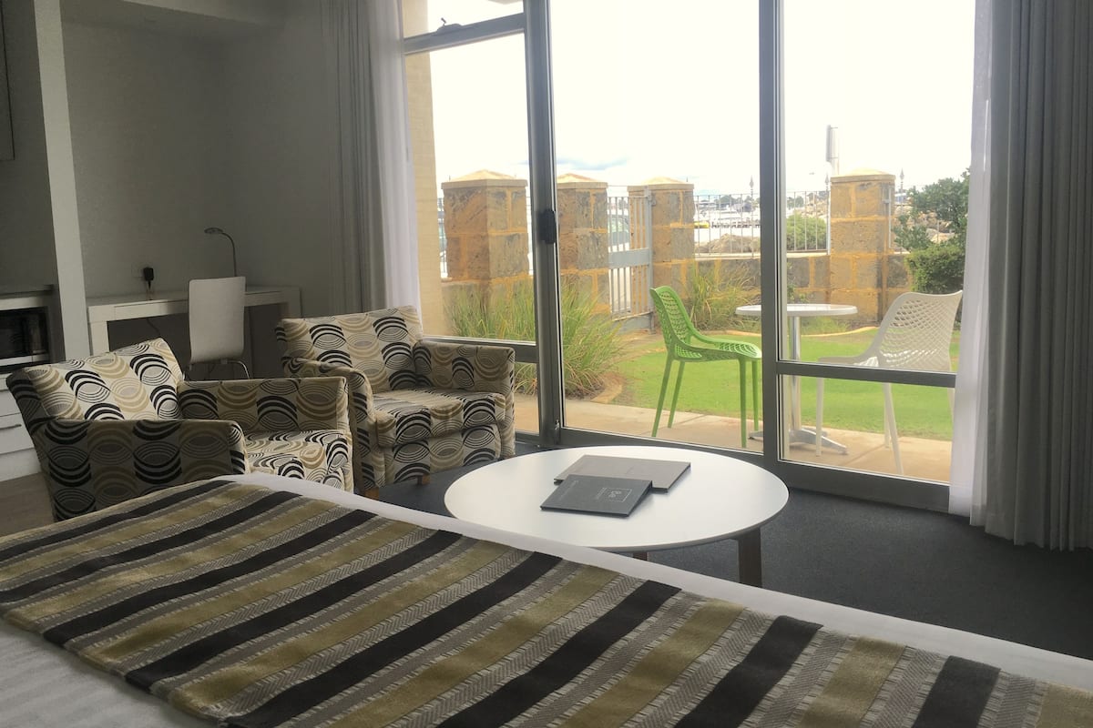 Una habitación de hotel moderna con un ventanal grande, un sofá, una mesa de comedor y una alfombra estampada.