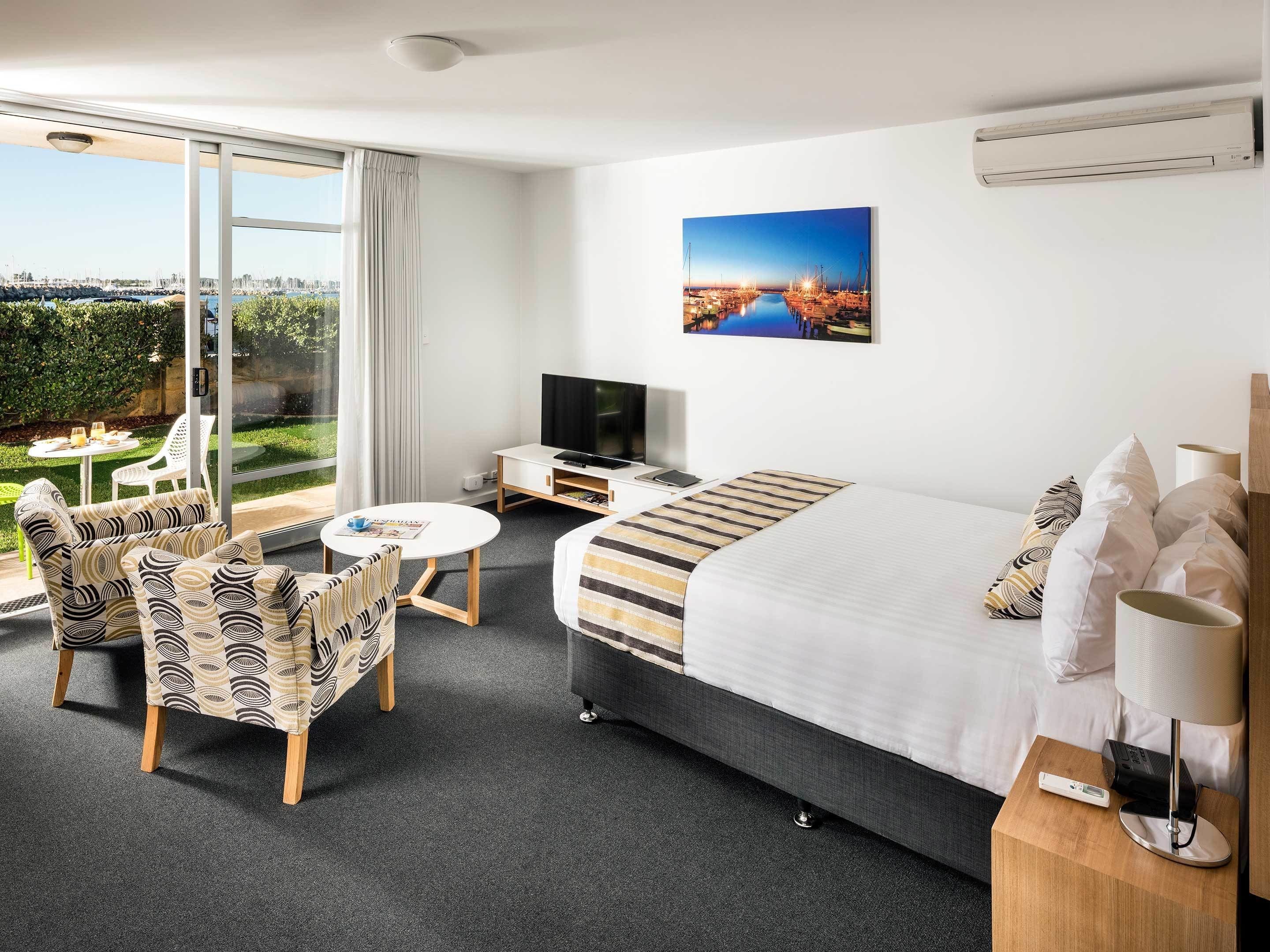 Habitación de hotel con una cama grande, televisión, escritorio y vistas a un puerto deportivo.