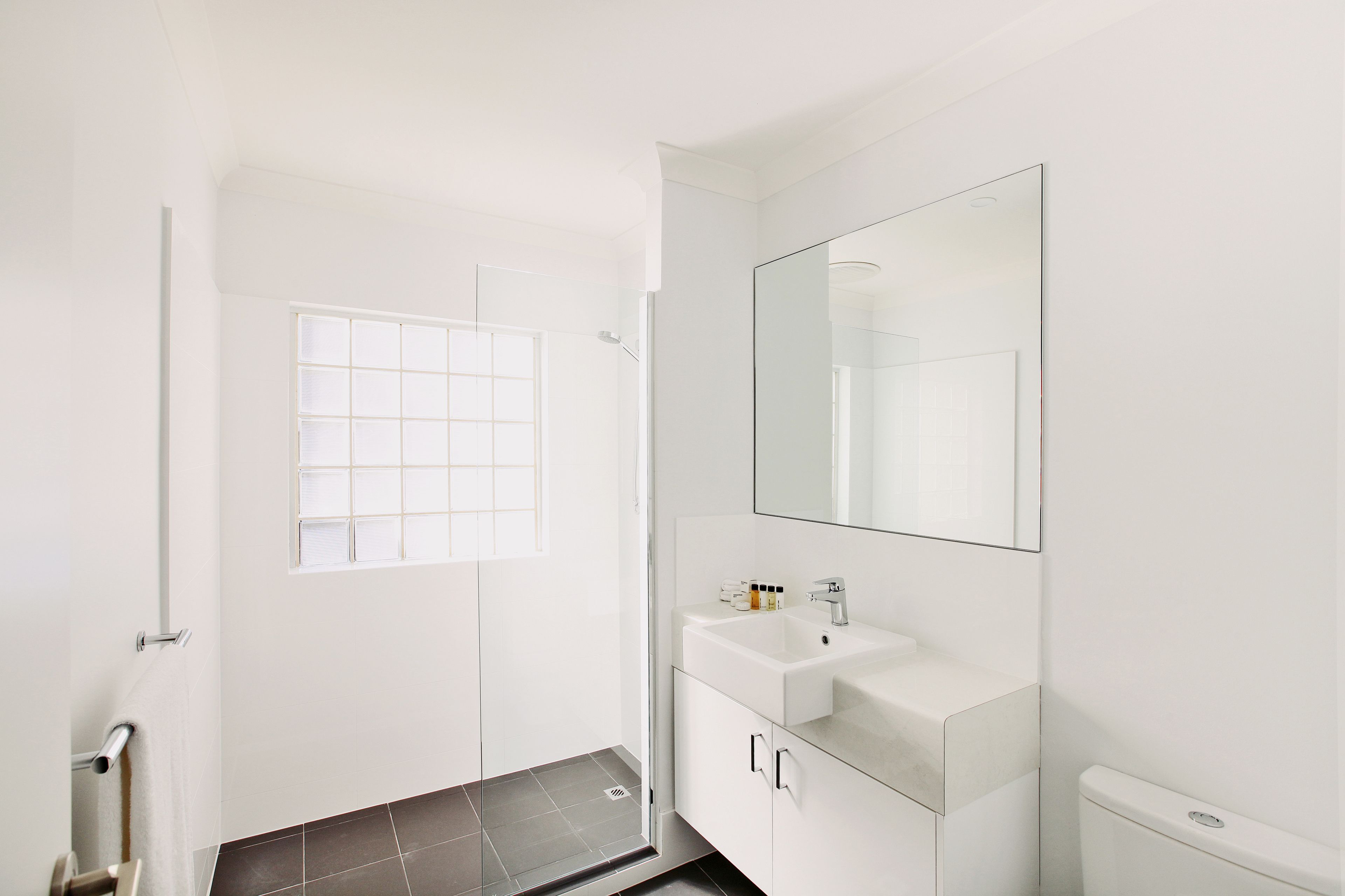 A modern bathroom with a white sink, mirror, and glass shower enclosure.