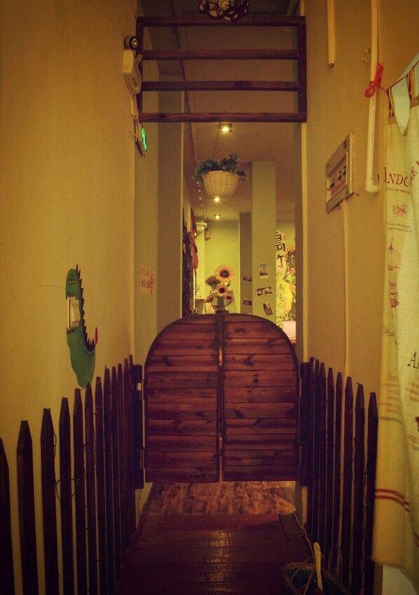 Un pasillo con una puerta de madera, una valla de madera a cada lado y una maceta colgante con flores.