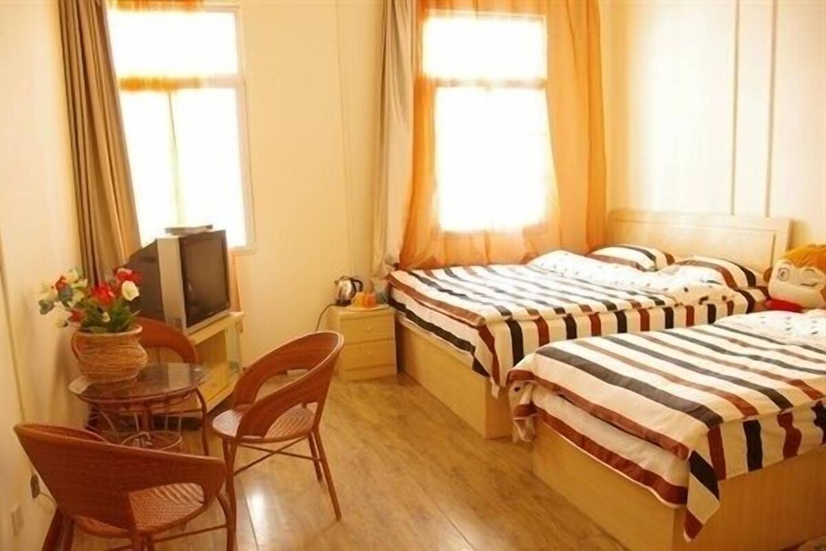 A hotel room with two beds, a TV, a small table with chairs, and a window with curtains.